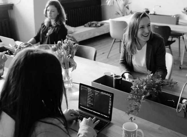 A photo of a bunch of people happily working on laptop computer. There's a purple filter on top of the photo.